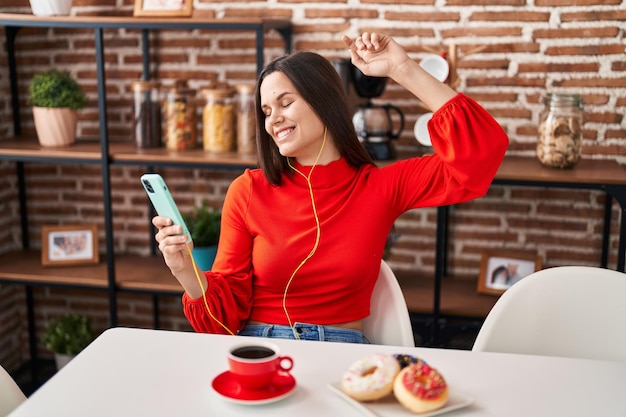 Giovane bella donna ispanica che ascolta la musica facendo colazione a casa