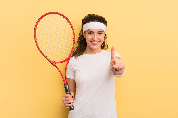 giovane bella donna ispanica che sorride con orgoglio e sicurezza facendo il numero uno. concetto di tennis