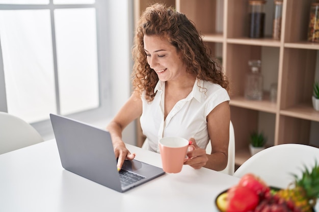 Giovane bella donna ispanica che usa il computer portatile che beve caffè a casa