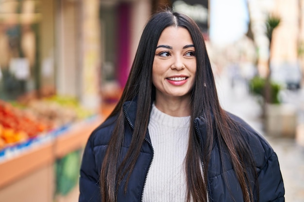 Giovane bella donna ispanica sorridente fiducioso guardando al lato della strada