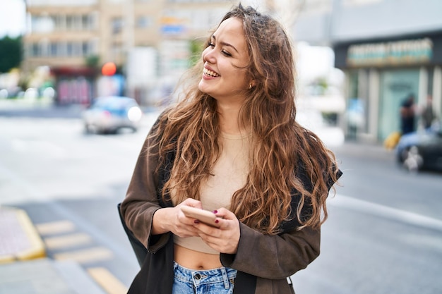 Giovane bella donna ispanica sorridente fiducioso utilizzando lo smartphone in strada