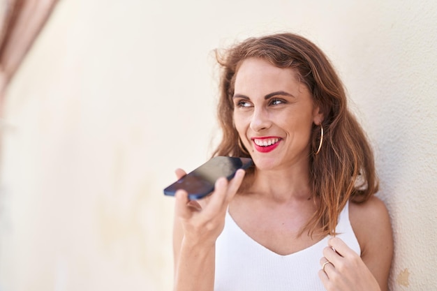 Giovane bella donna ispanica sorridente parlando fiducioso sullo smartphone in strada