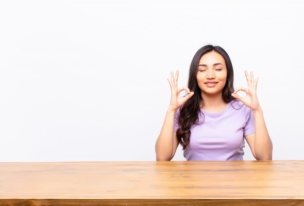 Giovane bella donna latina che sembra concentrata e meditando, sentendosi soddisfatta e rilassata, pensando o facendo una scelta contro la parete piatta