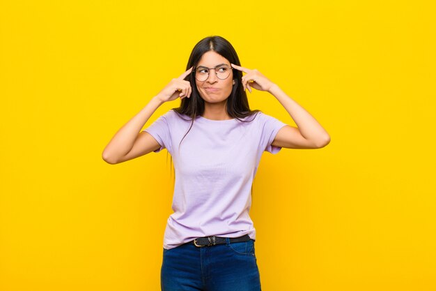 Giovane bella donna latina che sembra concentrata e pensa intensamente a un'idea, immaginando una soluzione a una sfida o un problema contro il muro piatto