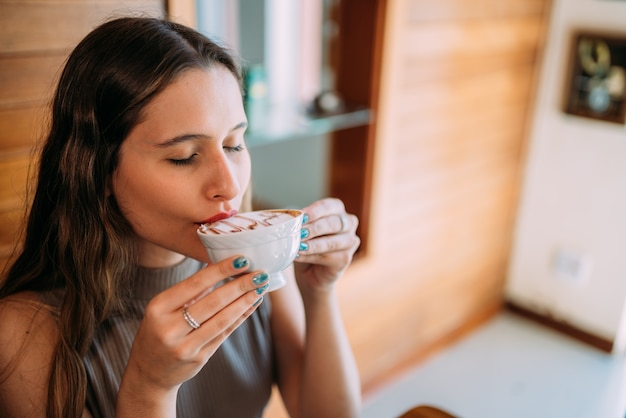 Giovane bella donna latina felice che gode del cappuccino in un caffè della via