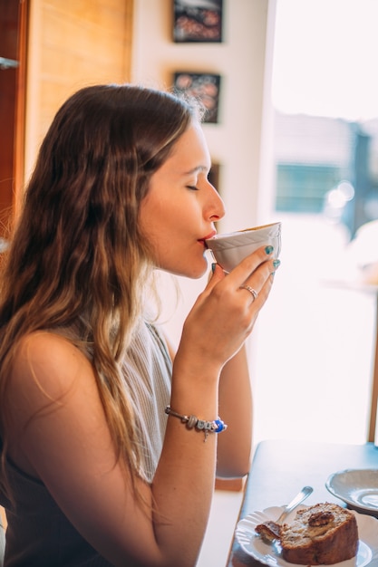 Giovane bella donna latina felice con lunghi capelli ricci che si gode un cappuccino in un caffè di strada