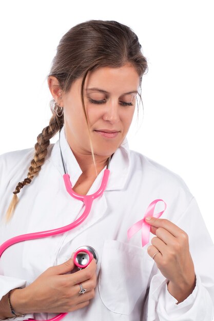 Giovane bella donna medico con stetoscopio rosa e nastro rosa di consapevolezza per il cancro al seno su un bianco.