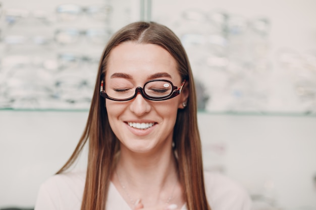 Giovane bella donna modello con gli occhiali per il trucco nell'ottico donna sorridente con gli occhiali per il trucco nel negozio di ottica