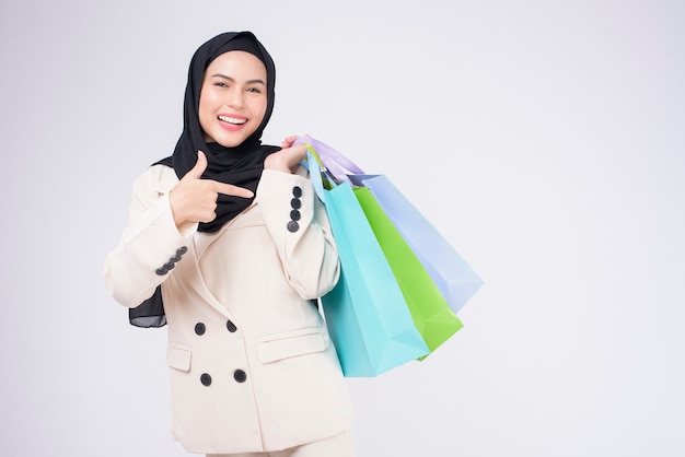 Giovane bella donna musulmana in vestito che tiene le borse della spesa colorate su sfondo bianco studio