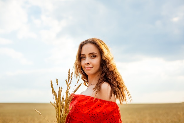 Giovane bella donna nel campo di grano dorato donna felice in vestito rosso che gode della vita nel campo natura b...