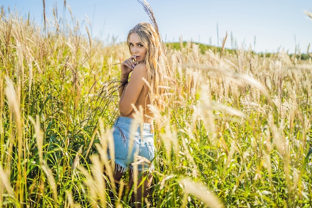 Giovane bella donna nel paesaggio autunnale con fiori secchi, spighe di grano. Moda autunno inverno. Autunno soleggiato, foto di moda.