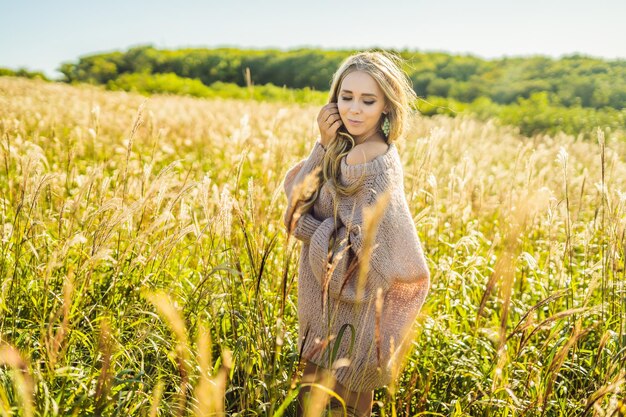 Giovane bella donna nel paesaggio autunnale con fiori secchi, spighe di grano. Moda autunno inverno. Autunno soleggiato, maglione autunnale accogliente. foto di moda