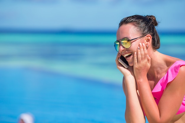 Giovane bella donna parla al telefono sulla spiaggia bianca