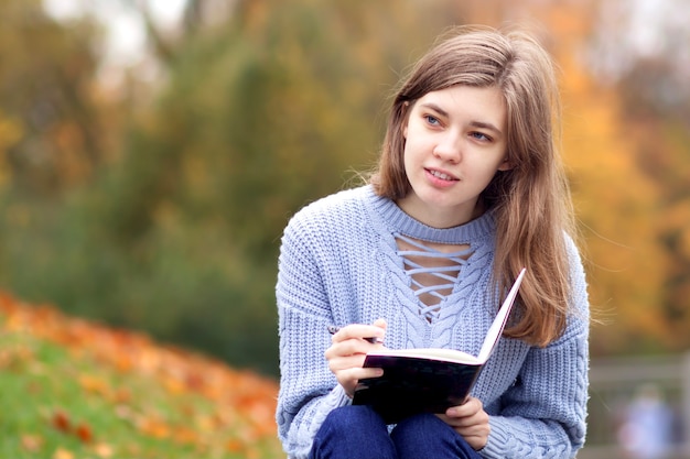 Giovane bella donna scrittrice, ragazza studentessa adolescente sta studiando all'aperto nel parco autunno dorato