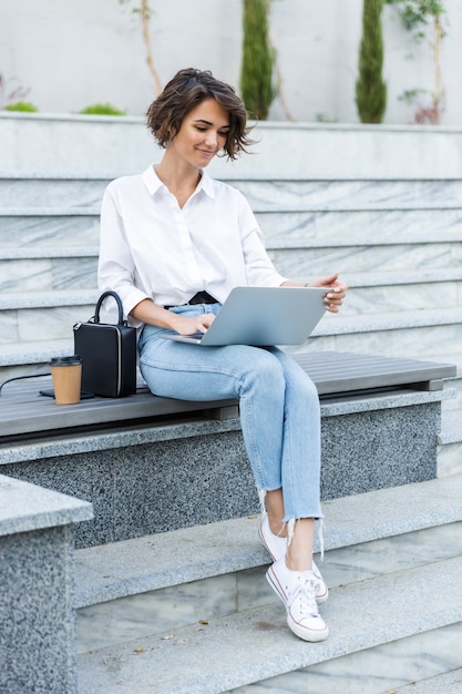 Giovane bella donna seduta all'aperto utilizzando il computer portatile