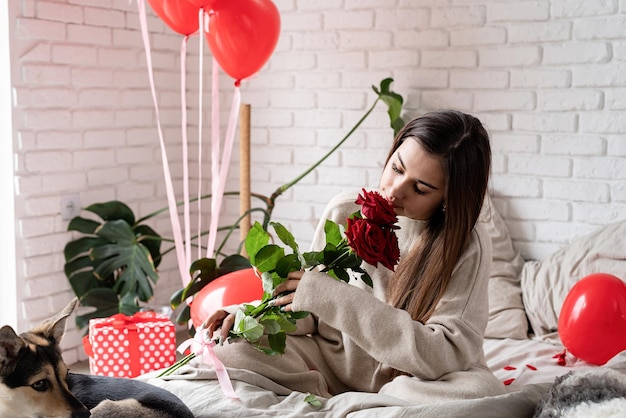 Giovane bella donna seduta nel letto per celebrare il giorno di San Valentino con rose rosse