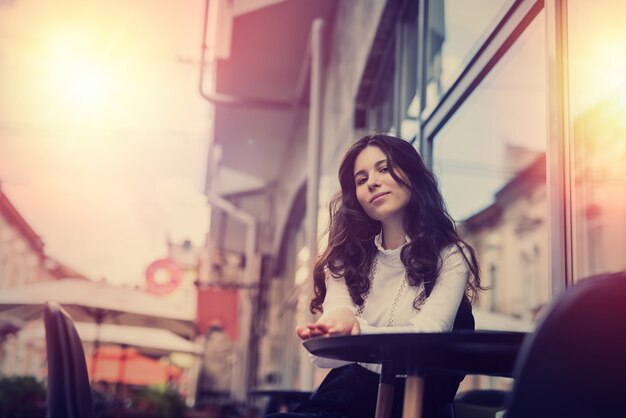 Giovane bella donna seduta vicino al caffè nel centro della città e in posa, goditi lo stile di vita estivo