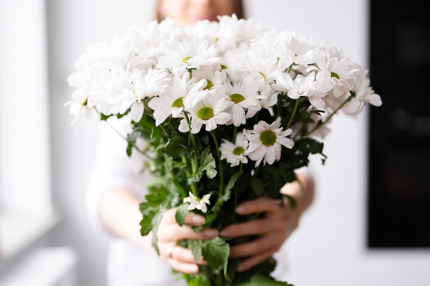 Giovane bella donna sorridente adorabile dolce sveglia con tenere un mazzo di fiori freschi bianchi a casa