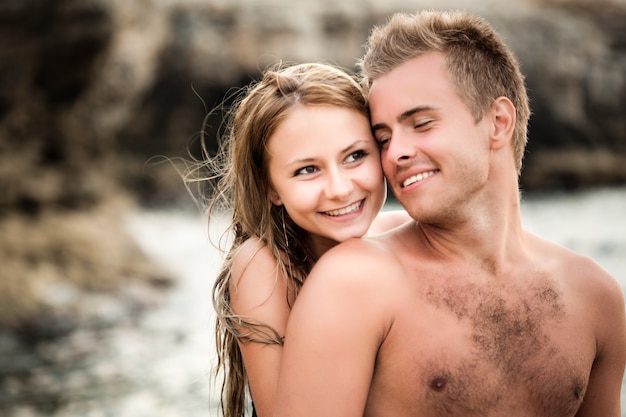 Giovane bella donna sorridente che abbraccia dalla parte posteriore il suo ragazzo felice con rocce naturali a sfondo in una limpida giornata estiva