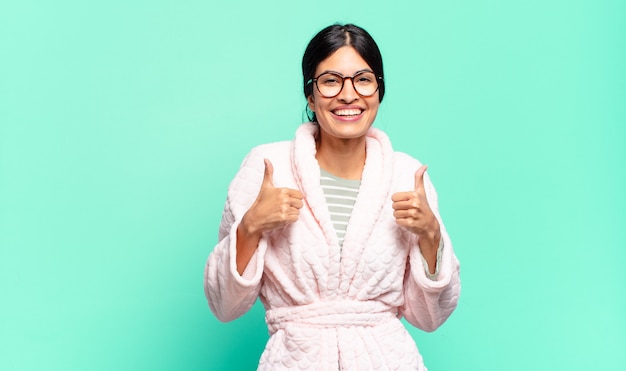 Giovane bella donna sorridente che sembra ampiamente felice, positiva, sicura di sé e di successo, con entrambi i pollici in su