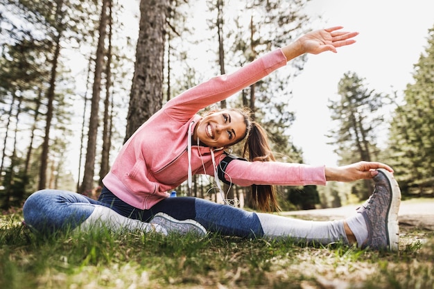 Giovane bella donna sorridente che si allunga dopo aver fatto jogging in natura.