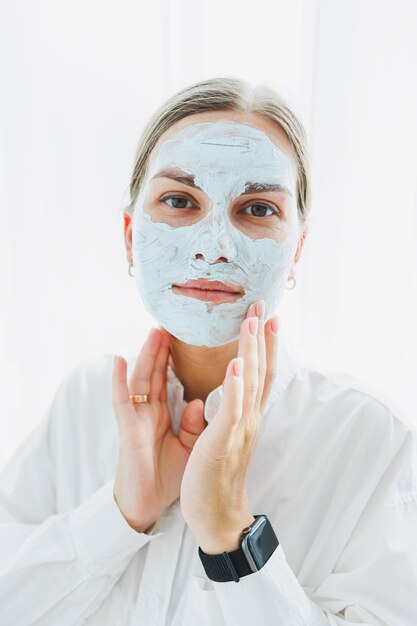 Giovane bella donna sorridente con la crema sul viso maschera di cura per la pelle del viso