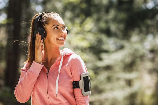 Giovane bella donna sorridente corridore che ascolta musica e si prende una pausa dopo aver fatto jogging nella natura.