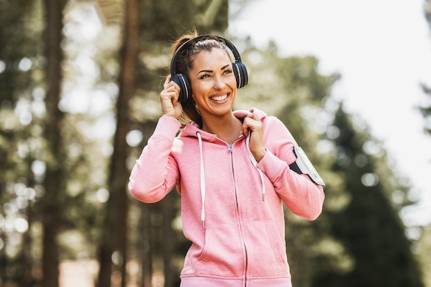 Giovane bella donna sorridente corridore che ascolta musica e si prepara a fare jogging nella natura.