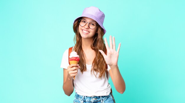 Giovane bella donna sorridente e dall'aspetto amichevole, mostrando il numero cinque in possesso di un gelato. concetto di estate