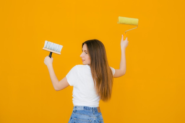 Giovane bella donna sorridente in abiti casual che tiene il rullo di vernice per la pittura murale isolata su y