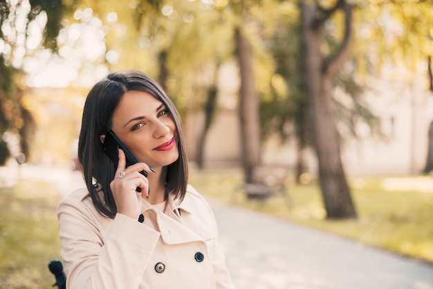 Giovane bella donna sorridente parlando sul cellulare nel parco.