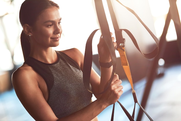 Giovane bella donna sportiva che regola le cinghie di fitness trx mentre ti alleni in palestra