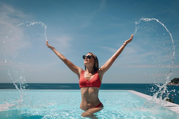 Giovane bella donna spruzzi d'acqua in piscina Bellissimo paesaggio marino. Viaggio a destinazione calda. Phuket. Tailandia.