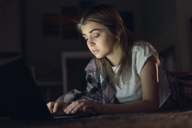 Giovane bella donna sta lavorando di notte a casa per un laptop