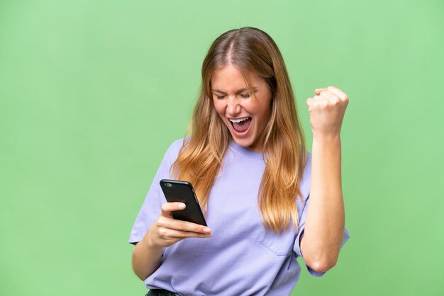 Giovane bella donna su sfondo isolato con il telefono in posizione di vittoria