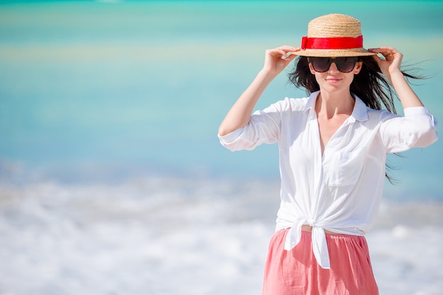 Giovane bella donna sulla spiaggia tropicale della sabbia bianca. Ragazza caucasica con cappello in abito bianco sullo sfondo del mare