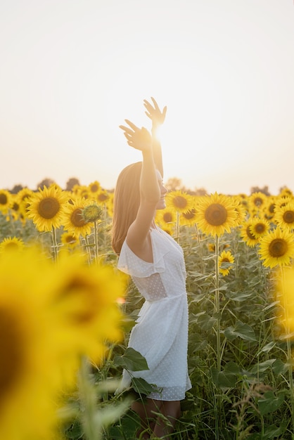 Giovane bella donna tra i girasoli al tramonto