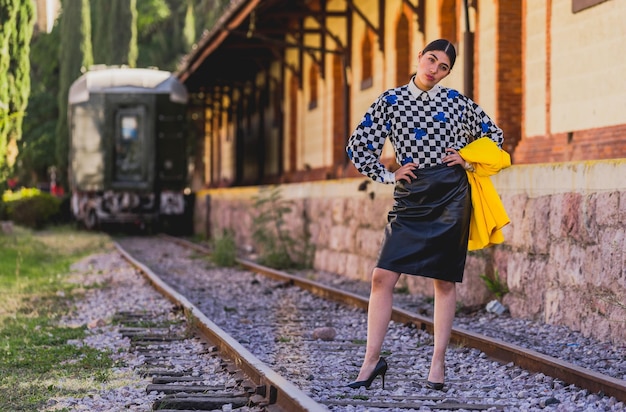 Giovane bella donna turistica in stile retrò nella vecchia stazione ferroviaria, indossa una giacca gialla e nera.