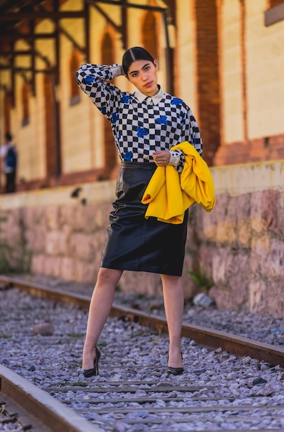 Giovane bella donna turistica in stile retrò nella vecchia stazione ferroviaria, indossa una giacca gialla e nera.