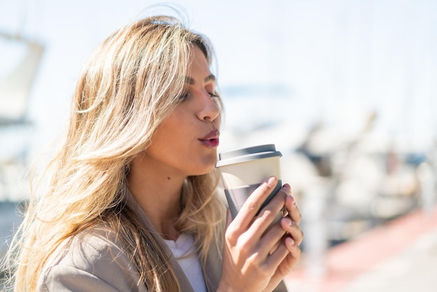 Giovane bella donna uruguaiana bionda all'aperto che tiene un caffè da asporto