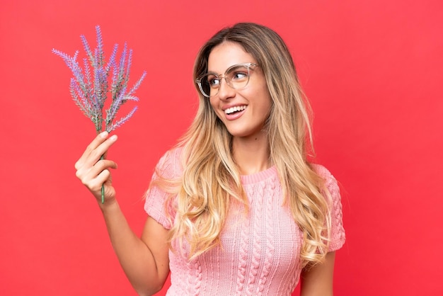 Giovane bella donna uruguaiana che tiene lavanda isolata su sfondo rosso con felice espressione