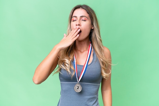 Giovane bella donna uruguaiana sportiva con medaglie su sfondo isolato che sbadiglia e copre la bocca spalancata con la mano
