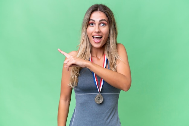 Giovane bella donna uruguaiana sportiva con medaglie su sfondo isolato sorpreso e puntando il lato