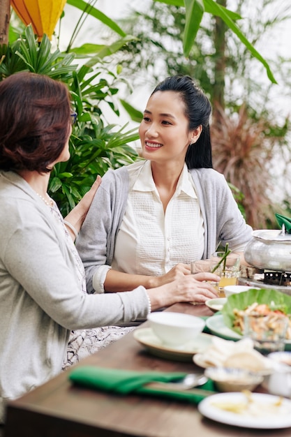 Giovane bella donna vietnamita a cena con la madre e discutendo di notizie