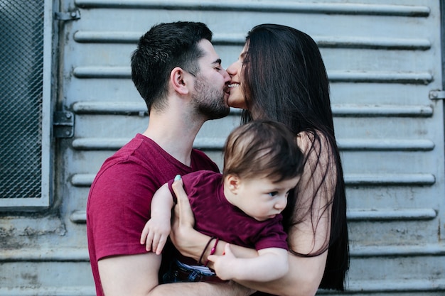 Giovane bella famiglia con bambino in posa sul muro grigio