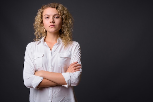 Giovane bella imprenditrice con capelli biondi ricci contro il grigio