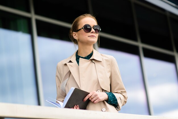 Giovane bella imprenditrice con occhiali da sole, telefono, laptop, tazza di caffè nelle strade della città.