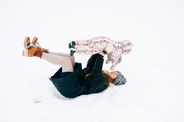 Giovane bella madre che gioca con la piccola figlia all'aperto in inverno. La femmina sorridente allegra felice con il bambino adorabile si diverte in neve.