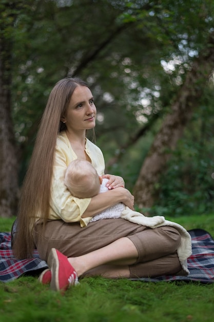 Giovane bella madre che tiene bambino e seduto su una coperta da picnic Cornice verticale