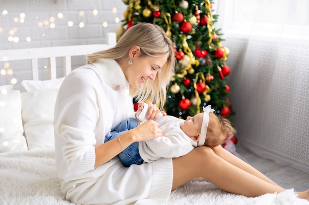 Giovane bella madre e bambino che celebrano il Natale a casa con un albero di Natale e decorazioni